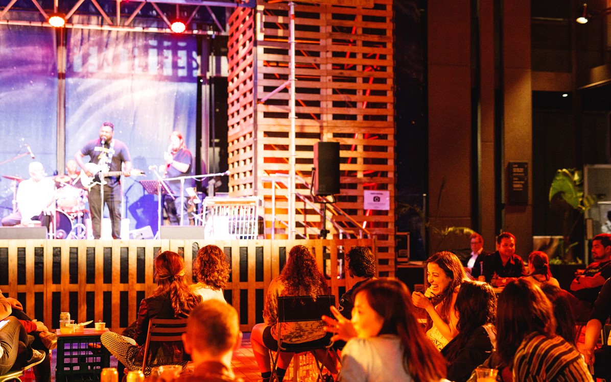 A crowd seated on folding chairs in front of a raised stage upon which a contemporary music band is performing. 