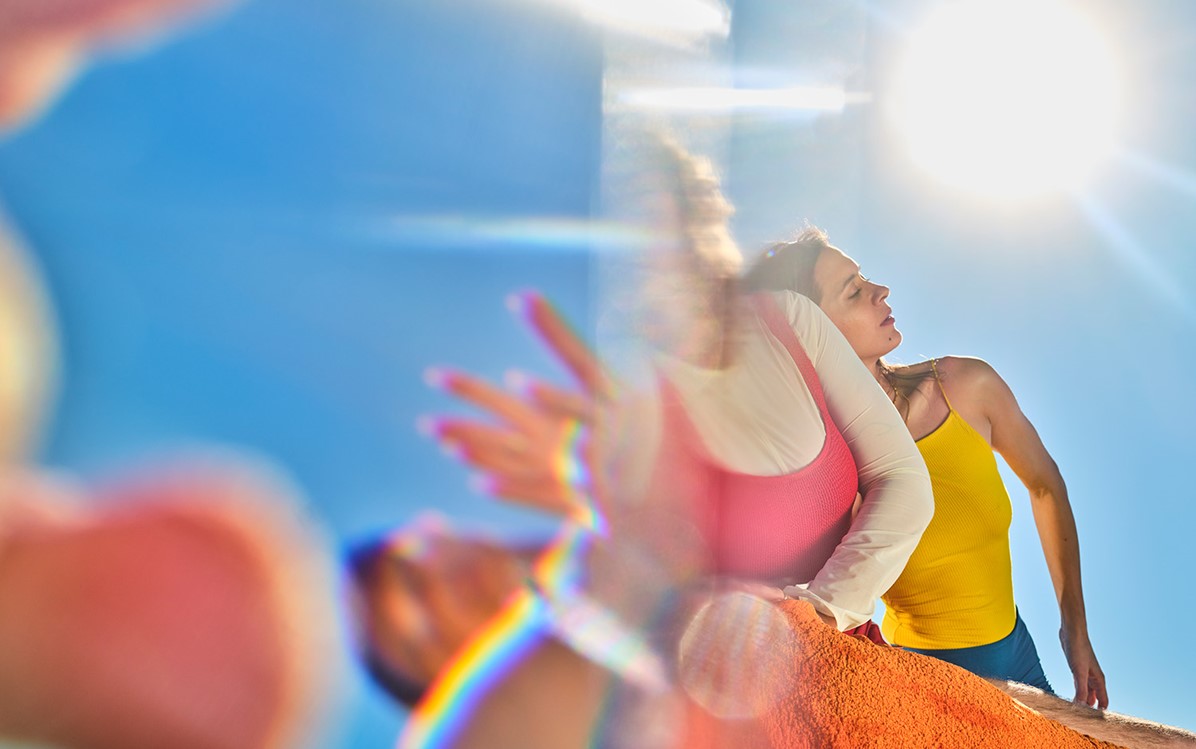 Dancers are posed looking down on the camera with a clear sky and sun behind them. The image is a little blurred from the sun