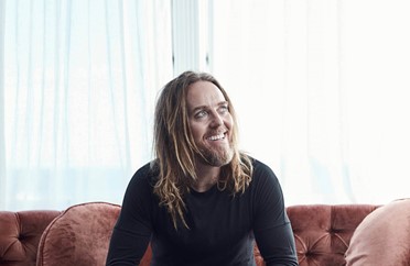 Image of Tim Minchin sitting on a couch and smiling