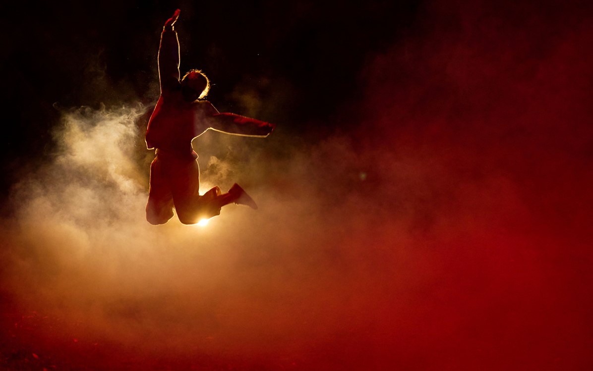 A dancer is jumper in the air surrounded by smoke. 