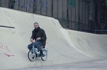 Image of a man sitting on a small bike on a skate ramp in the film Apples.