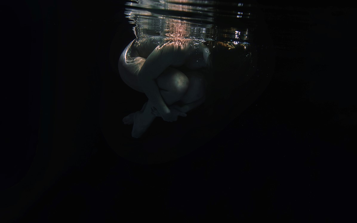 A seemingly nude person is pictured underwater in the foetal position.
