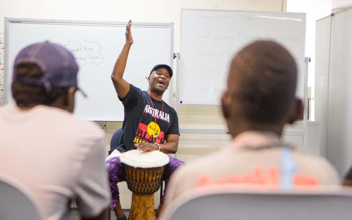 Image of a man with a bongo drum facing an audience in a classroom