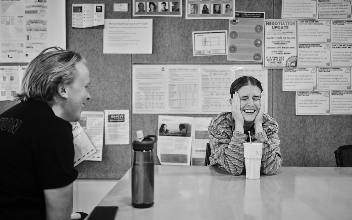 A black and white image of two people seated at a table talking and laughing.  Credit Duncan Wright