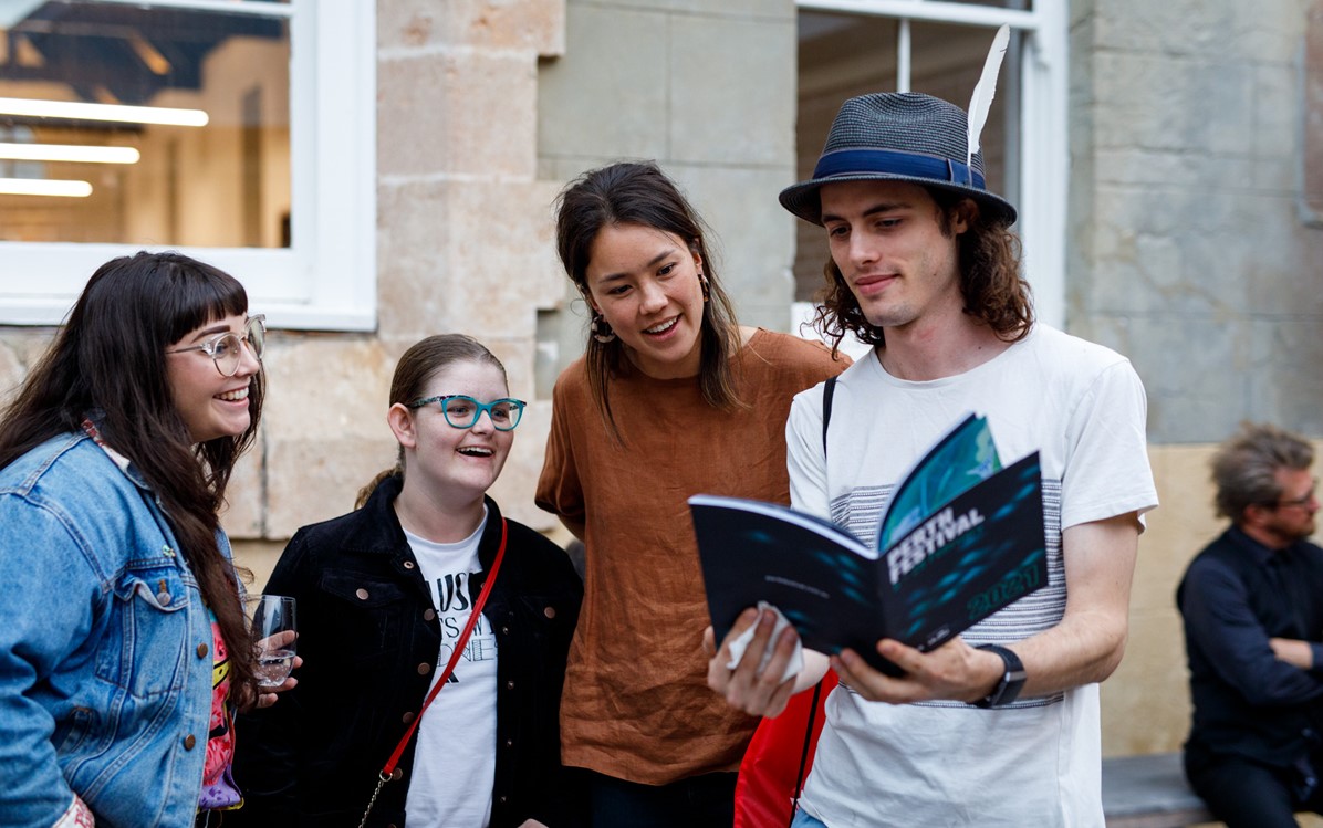A person in a hat opens the Perth Festival 2021 brochure, a group of three next to him look at open page.