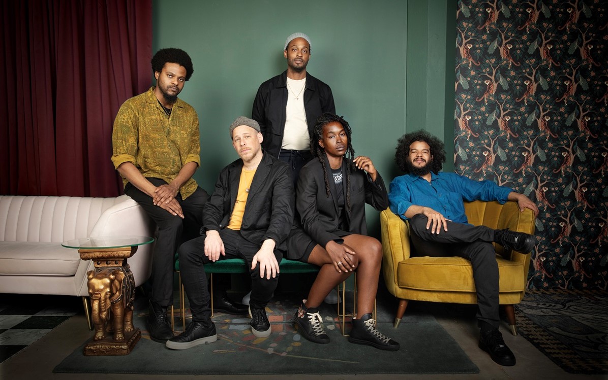 irreversible Entanglement posed together, four members are seated and the other two are either higher seated or standing in a living room setting