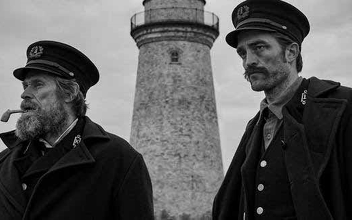 Image of two actors standing in front of a lighthouse from the film ''The Lighthouse''