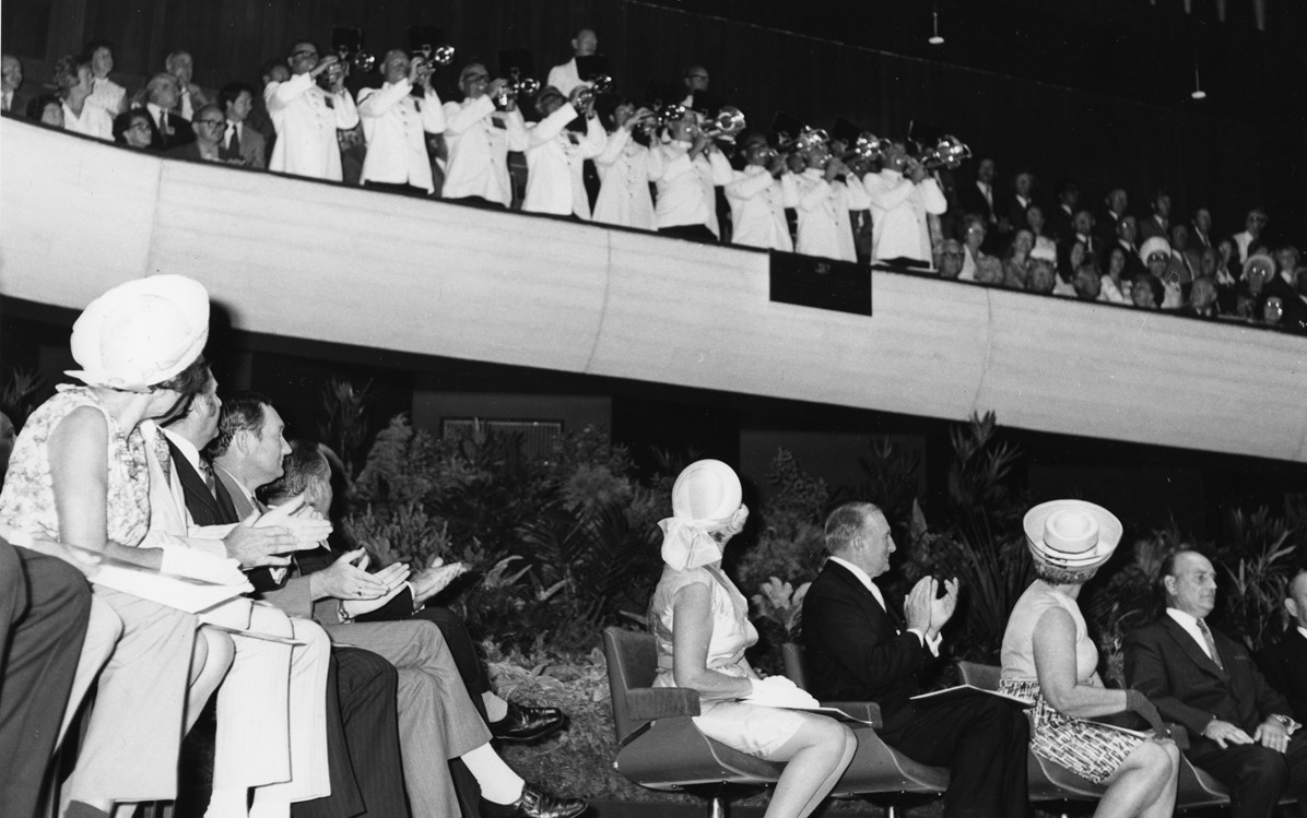 A black and white historic image of the official opening of the Perth Concert Hall in 1973. The audience is seated in the chairs clapping, looking up towards the first tier of seating where a trumpet band are playing. Credit City of Perth History Centre Collection