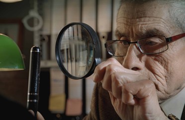 Image of undercover agent Sergio looking at an object with a magnifying glass in the film The Mole Agent.