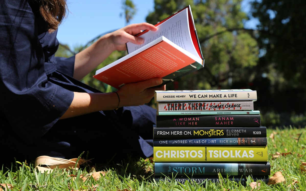 Image of a pile of books on grass and a lady reading one