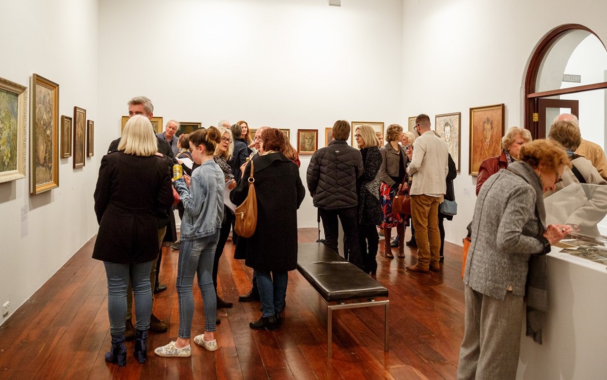 An exhibition room filled with people looking at the artwork.