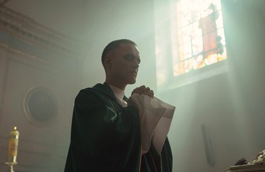 Image of Daniel wearing a robe and praying in a church in the film Corpus Christi.