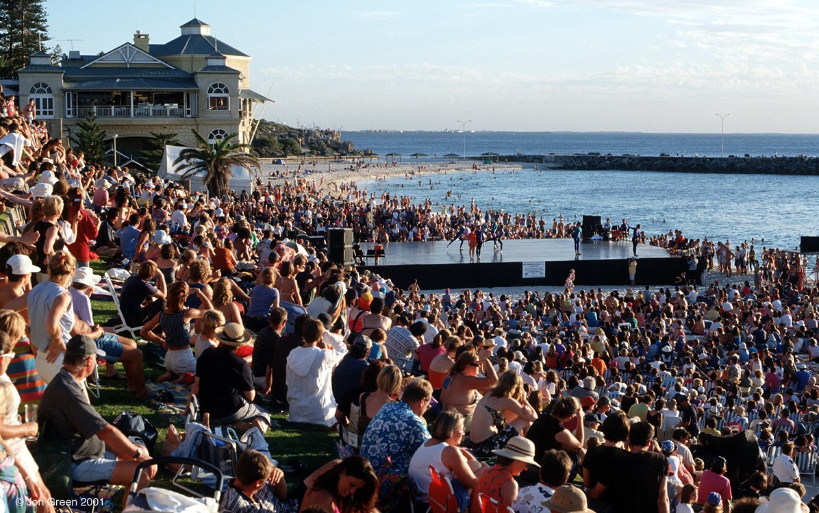 An image of Cottesloe beach packed with people and a stage is set up with a few dancers dancing on it.