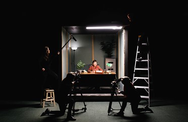 Image of cameramen in a dark room filming a person in a lit up box