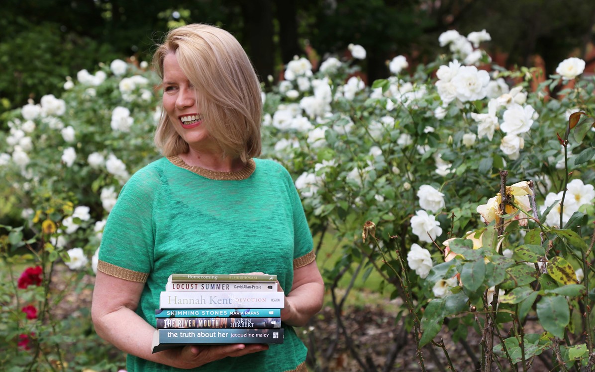 Gillian O'Shaughnessy holding books in front of rose bushes