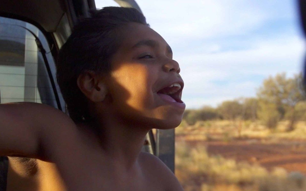 A child is pictured with their head out the side of a dual cab's window, mid-speech. From the film "In My Blood It Runs".