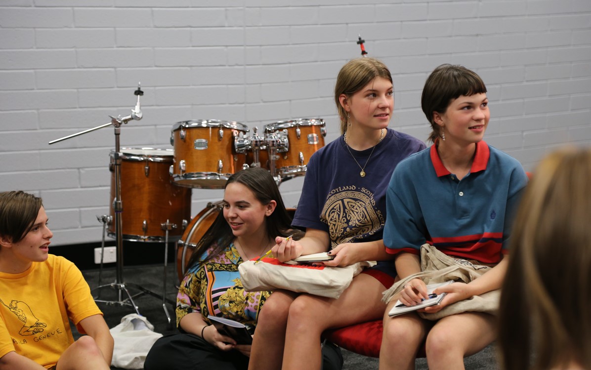 Image of 5 people sitting in a room with a drum set behind them 