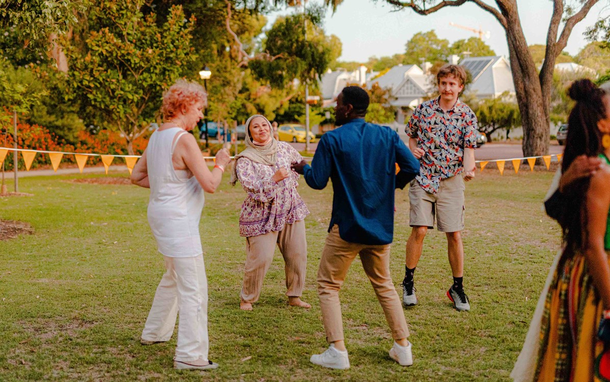 An image of four people dancing on a grassed area at sunset time