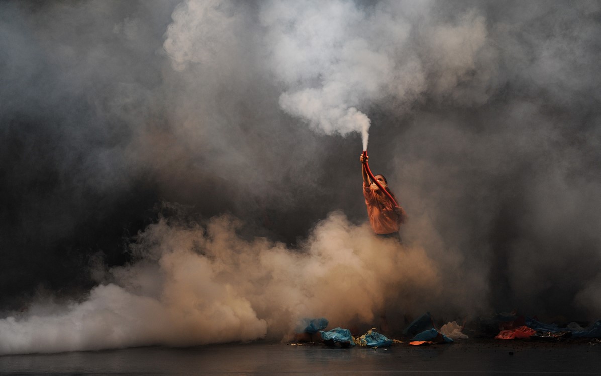 Performer holding out a pipe producing smoke, smoke surrounds them and the stage.