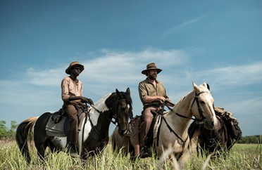 Image of Travis and Gutjuk riding horses in a field of tall grass in the film High Ground.