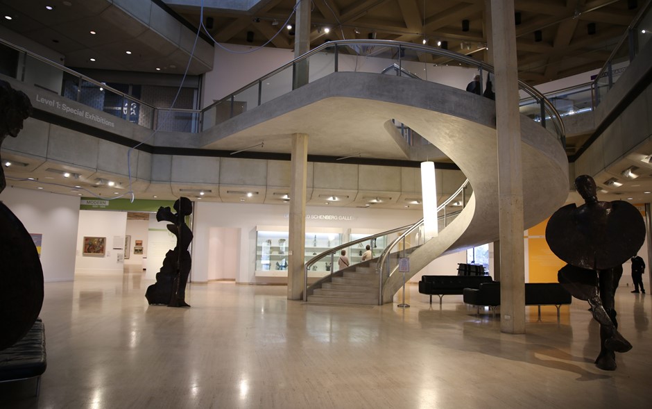 An image of the inside of the Art Gallery of Western Australia. The walls and celling are white with dark human like sculptures are scattered around the room with a winding central staircase.