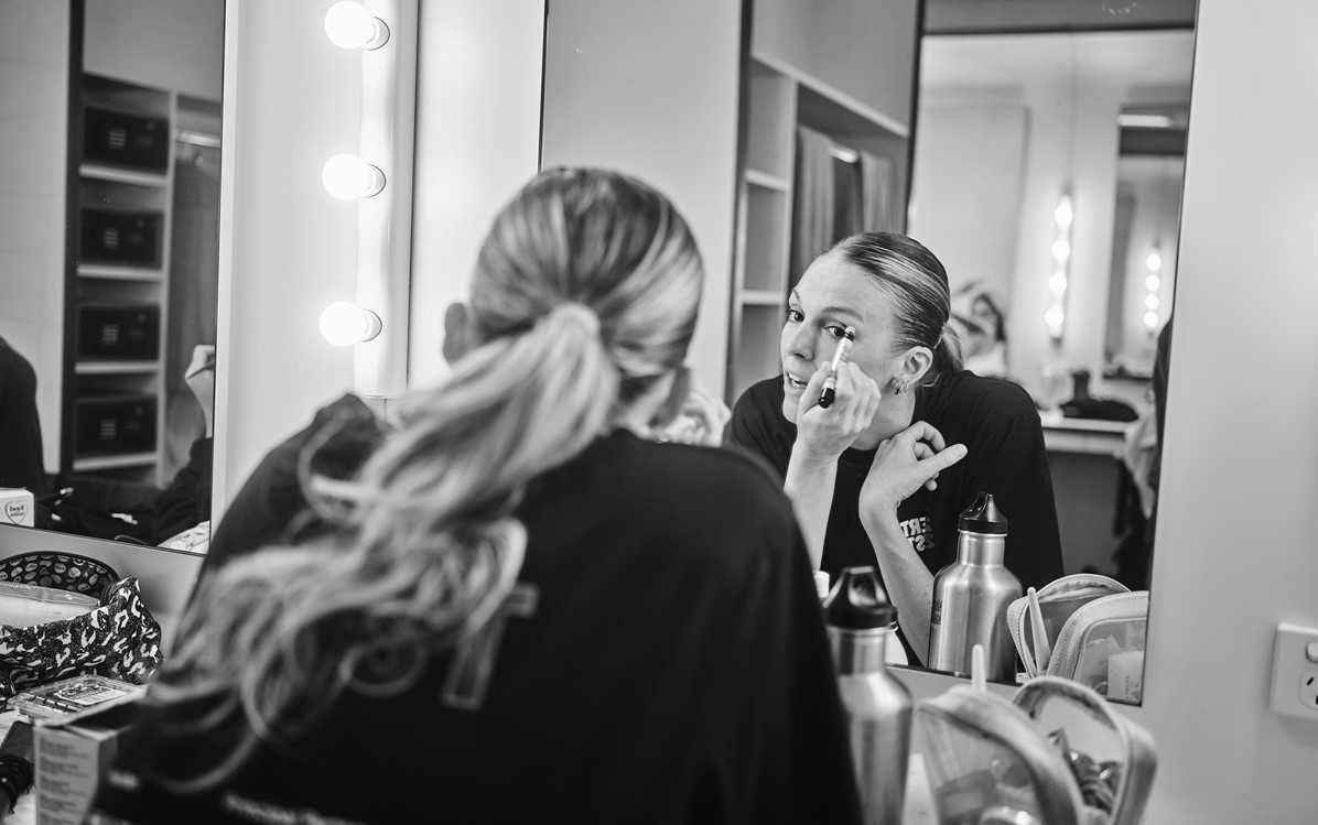 A black and white image of a performer putting make up on in a mirror.  Credit Duncan Wright